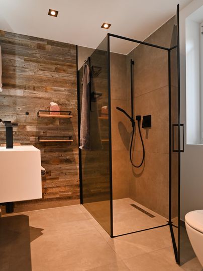 Ein modernes Badezimmer mit einer begehbaren Dusche und stilvollen Holzdetails. Die warmen Farbtöne schaffen eine einladende Atmosphäre.