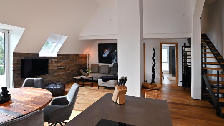 Ein modernes Wohnzimmer mit einem offenen Grundriss. Helle Farben, Holzfußboden und gemütliche Möbel schaffen eine einladende Atmosphäre.