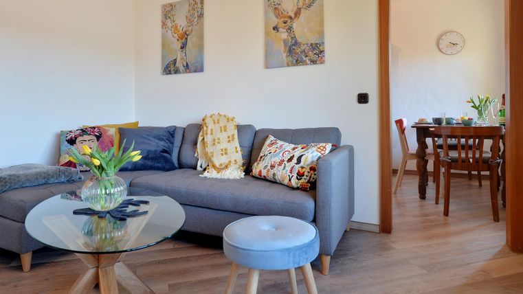 Een gezellige woonkamer met een grijze bank en een salontafel. Op de achtergrond zie je een eetgedeelte met een tafel en stoelen.