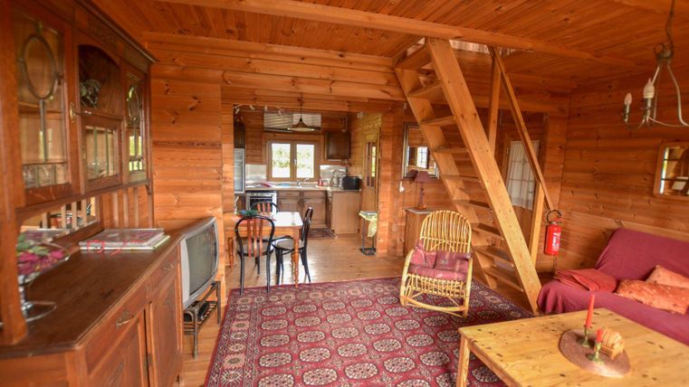 Un appartement en bois chaleureux avec un espace de vie ouvert. Il y a un escalier, une table basse et une kitchenette.