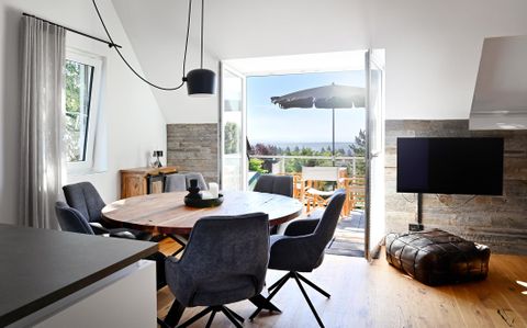 Een moderne eetkamer met een ronde houten tafel en comfortabele stoelen. Grote ramen bieden een uitzicht op het terras en het landschap.