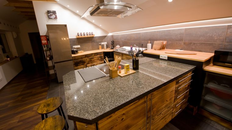 Eine moderne Küche mit einer großen Granitarbeitsplatte und Holzschränken. Die Räume sind gut beleuchtet und wirken einladend.