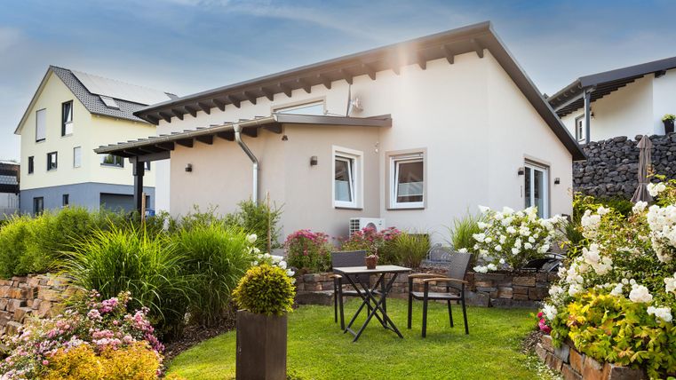 Ein charmantes Haus mit einem schönen Garten. Es gibt Blumen, Rasen und eine kleine Terrasse mit einem Tisch und Stühlen.
