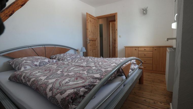 Ein gemütliches Schlafzimmer mit einem Doppelbett und Holzfußboden. Die Wände sind hell, und eine Tür führt zu einem weiteren Bereich.