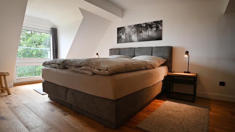 Ein modernes Schlafzimmer mit einem großen Bett und einem gemütlichen Holzboden. Das Zimmer hat viel Tageslicht und eine ruhige Atmosphäre.
