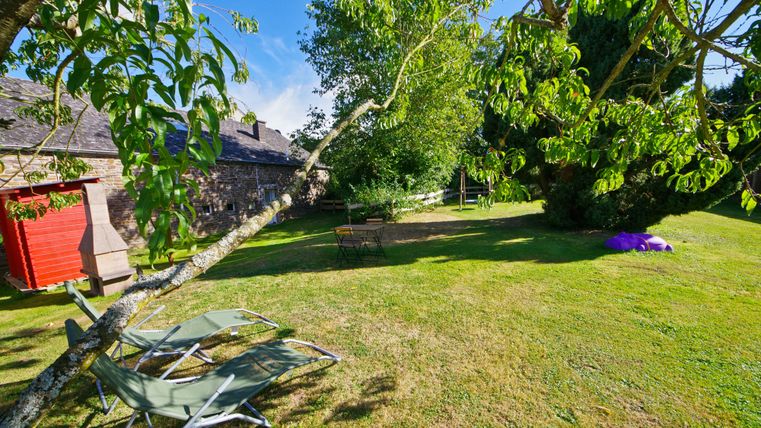 Ein ruhiger Garten mit grünem Rasen und zahlreichen Bäumen. Im Vordergrund stehen Liegen und im Hintergrund ist ein Gebäude sichtbar.