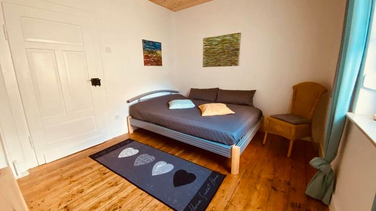 Ein gemütliches Schlafzimmer mit einem großen Bett und einem Stuhl. Die Wände sind mit bunten Bildern dekoriert und der Holzfußboden verleiht dem Raum eine warme Atmosphäre.