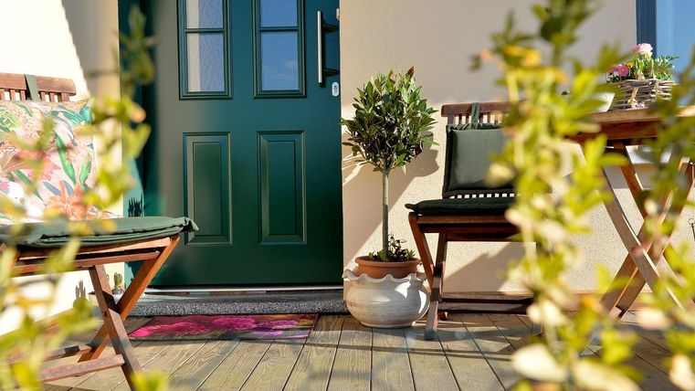 Een uitnodigende entree met een groene deur en houten meubels. Planten en een deurmat geven de ruimte een vriendelijke uitstraling.