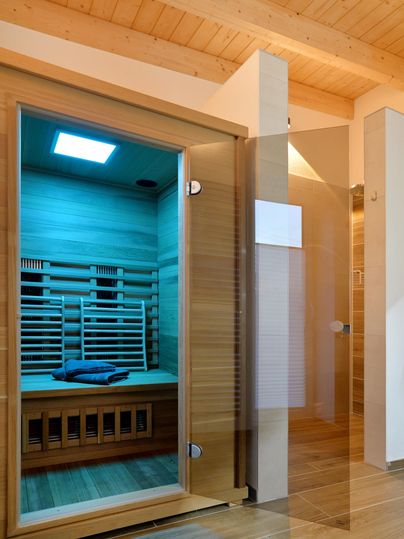 Eine moderne Sauna mit Holzelementen und einer gläsernen Tür. Der Raum ist hell und einladend gestaltet.