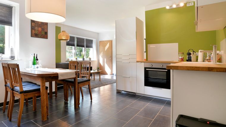 Eine moderne Küche mit einem Essbereich aus Holz. Die Wände sind in einem frischen Grünton gestrichen und das Licht ist hell.