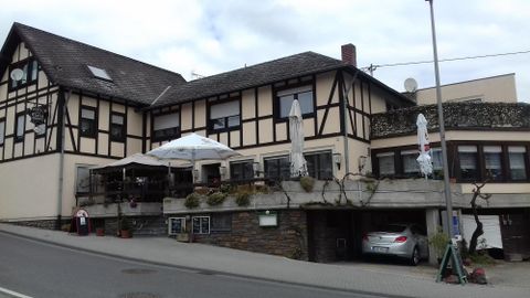 Ein traditionelles Fachwerkhaus mit einem Restaurantbereich und einer Terrasse. Vor dem Gebäude stehen einige Tische und ein Auto ist geparkt.