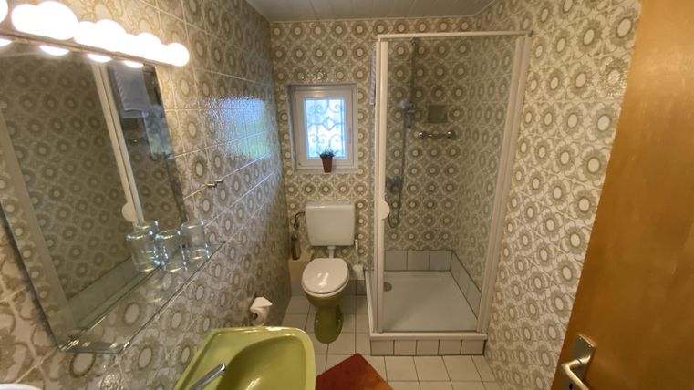 Ein kleines Badezimmer mit einer Dusche, Toilette und einem Waschbecken in einer grünen Farbe. Die Wände sind mit einem vintage Muster dekoriert.