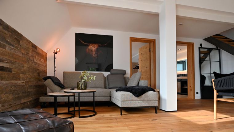 Ein modernes Wohnzimmer mit einer gemütlichen Couch und einem Holzfußboden. An der Wand hängt ein Kunstwerk, und es gibt viel natürliches Licht.