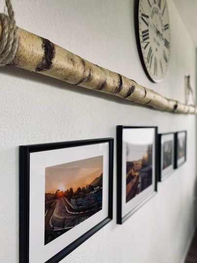 Eine stilvolle Wand mit einer Holzleiste und gerahmten Fotos. An der Wand hängt auch eine römische Uhr.
