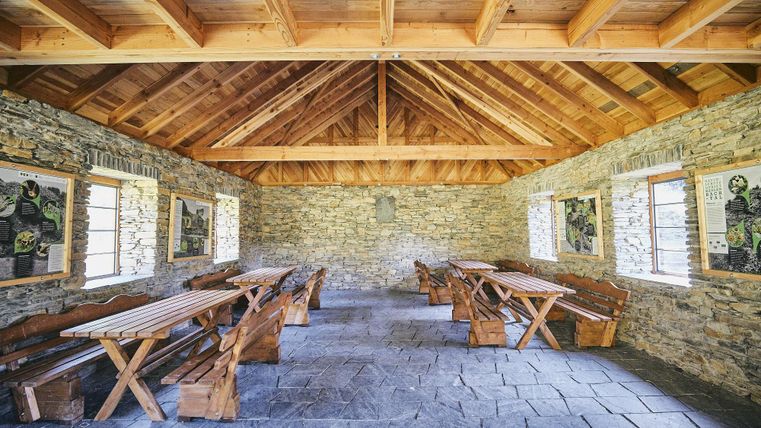 Ein gemütlicher Raum mit Holzverkleidung und steinernen Wänden. Holztische und Bänke laden zum Verweilen ein.