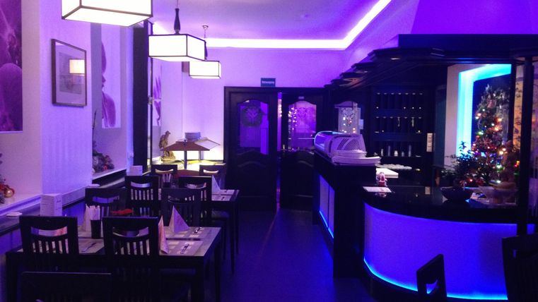 Ein elegantes Restaurant mit dunklen Möbeln und einer stilvollen Beleuchtung in lila Tönen. Die Bar ist gut ausgestattet und die Atmosphäre wirkt einladend und modern.