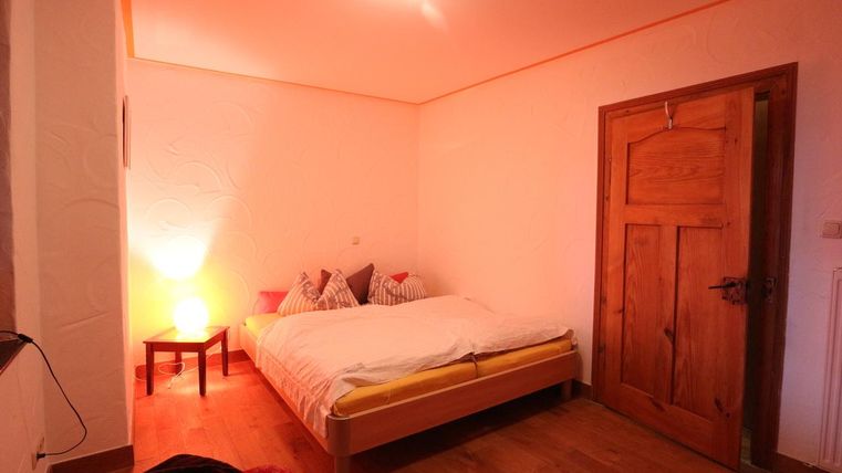 Ein gemütliches Schlafzimmer mit einem Doppelbett und Holzfußboden. Es gibt eine Nachttischlampe und einen Holzschrank.