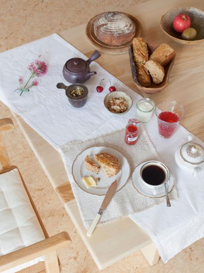 Une table accueillante dressée avec un petit-déjeuner. Il y a du pain, de la confiture, du thé et des fruits frais.