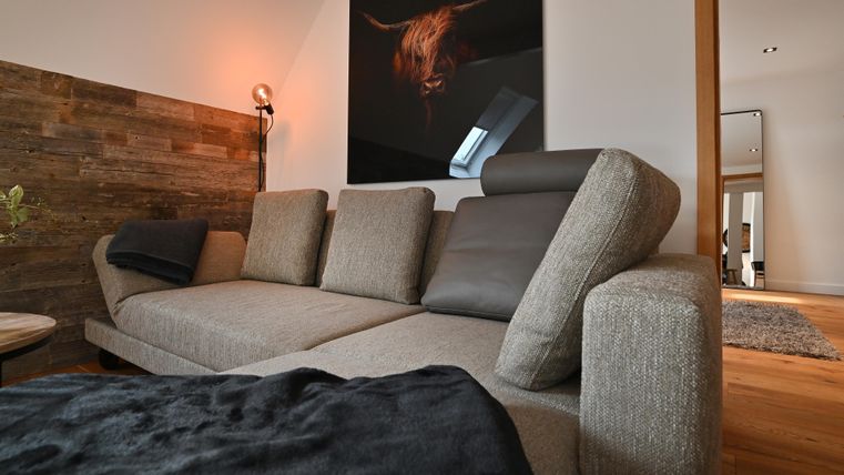 Ein modernes Wohnzimmer mit einem beigen Sofa und einer Holzwand. Im Hintergrund ist ein Kunstwerk eines Tieres zu sehen.