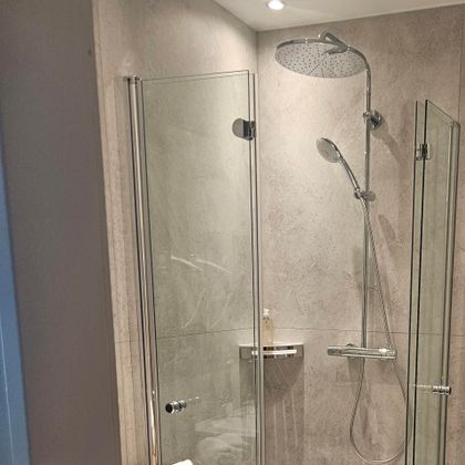 Eine moderne Duschkabine mit Glastüren und Regenbrause. Der Raum wirkt hell und sauber, mit einem minimalistischen Design.