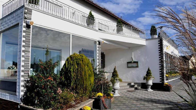 Ein modernes Gebäude mit einem einladenden Eingangsbereich. Umgeben von gepflegten Pflanzen und Blumen in Töpfen.