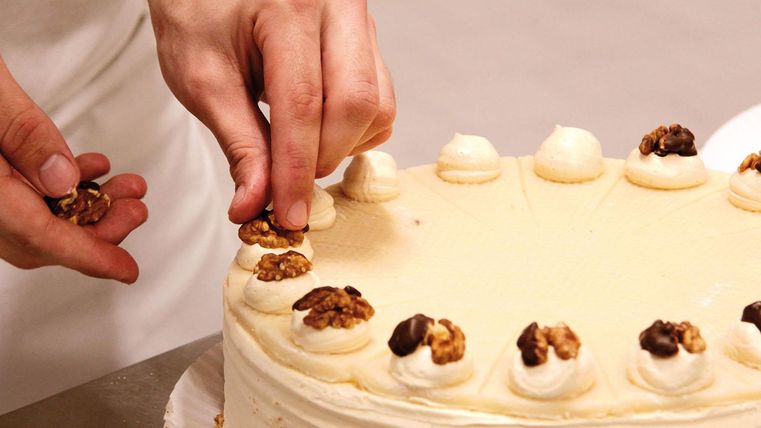 Eine Torte wird dekoriert. Jemand fügt Nüsse und Sahne oben hinzu.