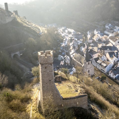 Luftaufnahme von Monreal mit einer Burg im Vordergrund und Fachwerkhäusern im Tal. Die Landschaft ist von Bäumen und Hügeln umgeben., © Eifel Tourismus GmbH, D. Ketz