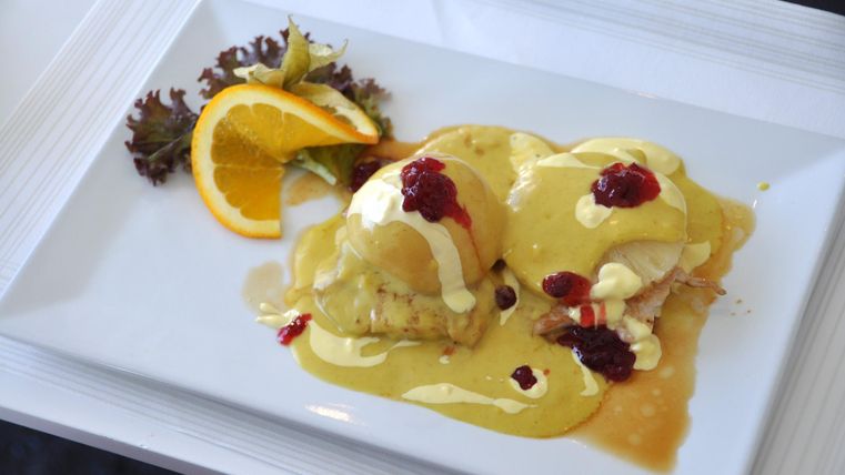 Ein köstliches Gericht mit pochierten Eiern, überzogen mit einer cremigen Sauce. Neben dem Essen liegen eine Orangenscheibe und ein wenig Salat.