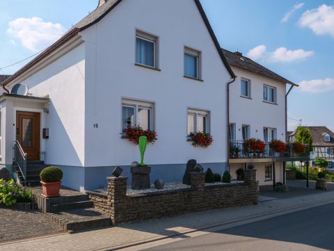 Een modern woonhuis met lichte muren en kleurrijke bloembakken. De straat is geplaveid en er is een klein tuin gedeelte.