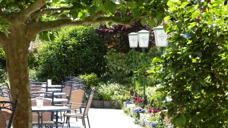 Ein einladender Garten mit Tischen und Stühlen lädt zum Verweilen ein. Umgeben von üppigem Grün und bunten Blumen bietet der Ort eine entspannte Atmosphäre.