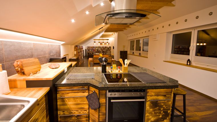 Eine moderne Küche mit Holz- und Steinelementen. Sie ist gut beleuchtet und hat große Fenster für viel Tageslicht.