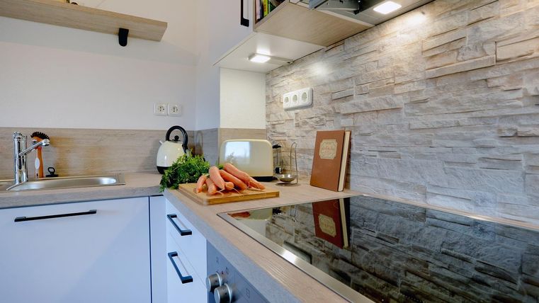 Een moderne keuken met een gladde kookplaat en een decoratieve stenen muur. Op het aanrecht liggen verse wortelen en verse kruiden.