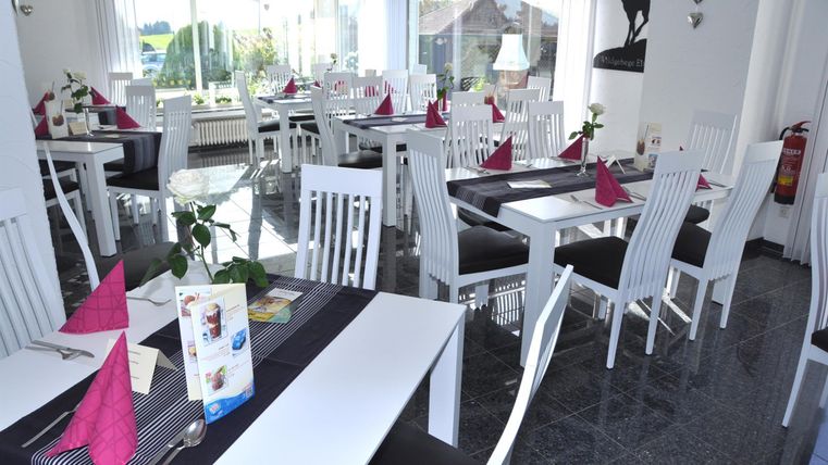 Ein modernes Restaurant mit weißen Tischen und Stühlen. Die Tische sind elegant mit lila Servietten und kleinen Pflanzen dekoriert.