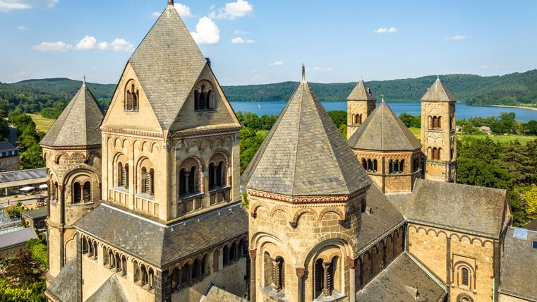 Eine beeindruckende Kirche mit spitzen Türmen und einer schönen Architektur. Im Hintergrund ist eine grüne Landschaft und ein Gewässer zu sehen.