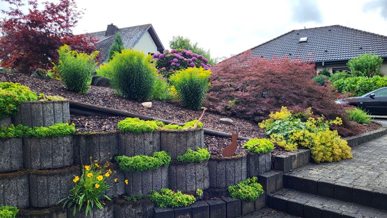 Ein schön gestalteter Garten mit bunten Pflanzen und Sträuchern. Die gestuften Beete aus Stein fügen sich harmonisch in die Landschaft ein.
