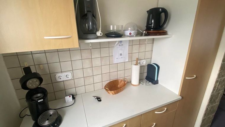 Eine kleine Küche mit verschiedenen Geräten auf einer weißen Arbeitsfläche. Es gibt eine Kaffeemaschine, einen Wasserkocher und eine dekorative Schüssel.