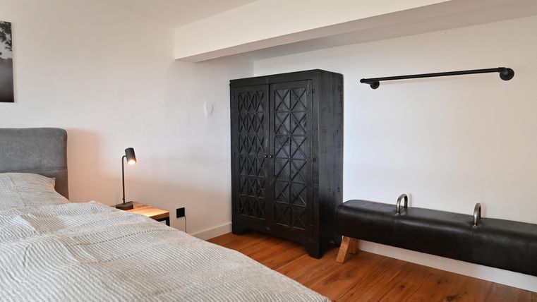 Ein modernes Schlafzimmer mit einem gemütlichen Bett, einem schwarzen Schrank und einem Holzfußboden. Eine stehlampe verleiht dem Raum eine warme Atmosphäre.