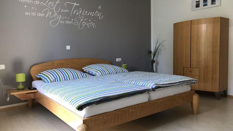 Ein gemütliches Schlafzimmer mit einem Holzbett und gestreiften Bettwäsche. An der Wand steht ein inspirierendes Zitat, und im Raum gibt es einen Kleiderschrank sowie eine Pflanze.