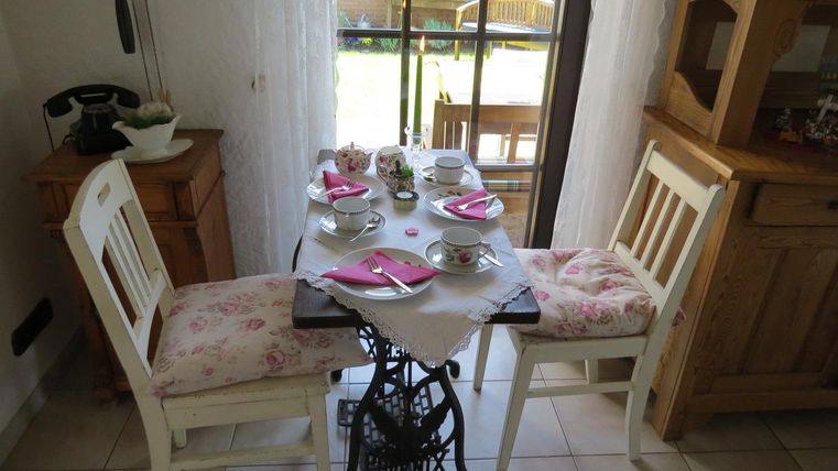 Ein gemütlicher Tisch mit zwei Stühlen, gedeckt für eine Teestunde. Auf dem Tisch stehen Teetassen und Teller mit rosa Servietten.