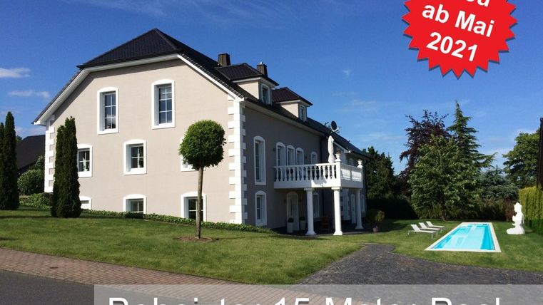 Ein modernes Haus mit einem gepflegten Garten und einem beheizten 15-Meter-Pool. Die Umgebung ist grün und einladend.