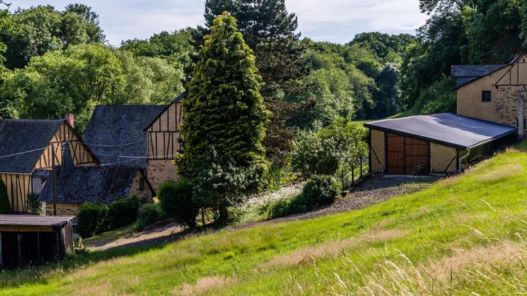 Un paysage pittoresque avec des maisons à colombages traditionnelles et beaucoup de verdure. À l'arrière-plan, on peut voir des arbres et une douce collline.