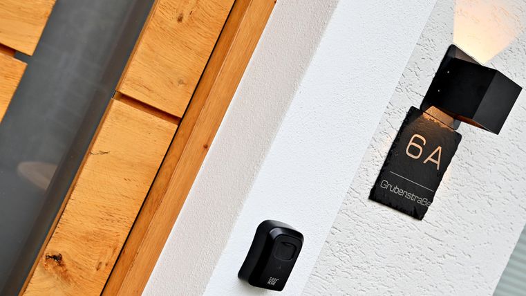 Eine moderne Hausnummer 6A ist an der weißen Wand angebracht. Neben der Hausnummer befindet sich eine schlichte Schwarz-Weiß-Türglocke.