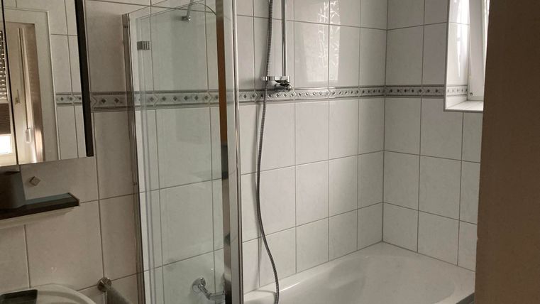 Ein Badezimmer mit einer Badewanne und einer Duschkabine. Die Wände sind mit weißen Fliesen gefliest und es gibt einen Spiegel.