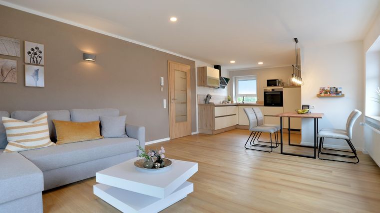 Ein modernes Wohnzimmer mit einem bequemen Sofa und einem Esstisch. Die offene Küche ist elegant und gut ausgestattet.