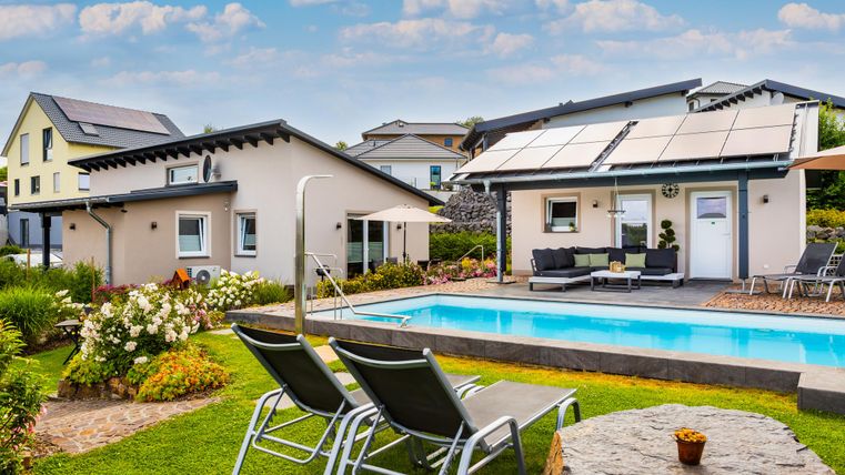 Ein modernes Haus mit einem Pool und Liegen im Garten. Gut gestaltete Außenanlagen mit Blumen und Sonnenschirmen.