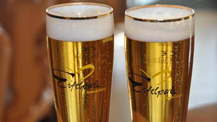 Zwei Gläser Bier mit cremigem Schaum und blassem Goldton stehen nebeneinander. Die Gläser sind mit dem Schriftzug „Eifelperle“ versehen.