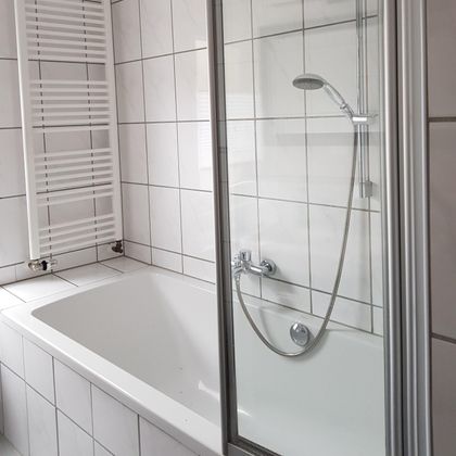 Ein modernes Badezimmer mit einer Badewanne und einer Duschabtrennung aus Glas. Die Wände sind gefliest und der Raum wirkt hell und sauber.