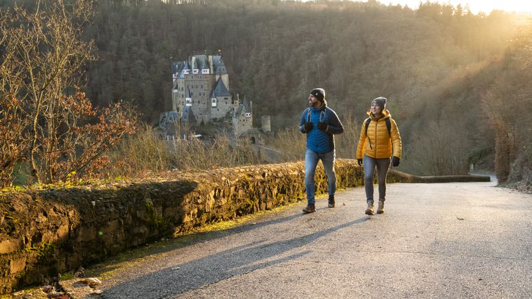 Zwei Wanderer auf einem Weg mit Burg Eltz im Hintergrund.