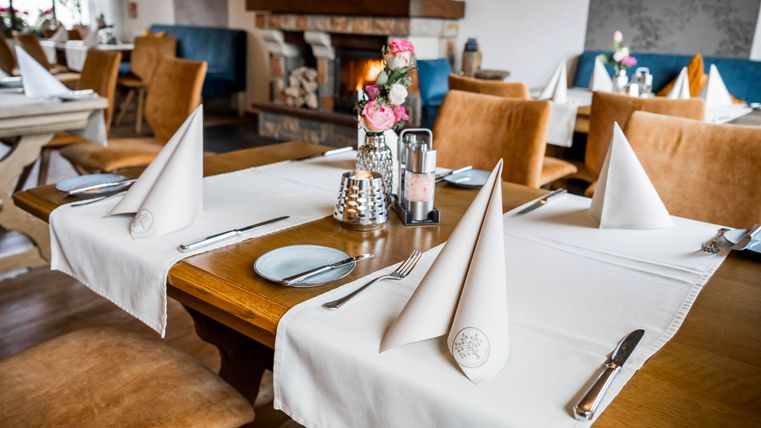 Een elegante tafel in een restaurant, liefdevol gedekt met witte servetten en bestek. Op de achtergrond zorgt een gezellige open haard voor een aangename sfeer.