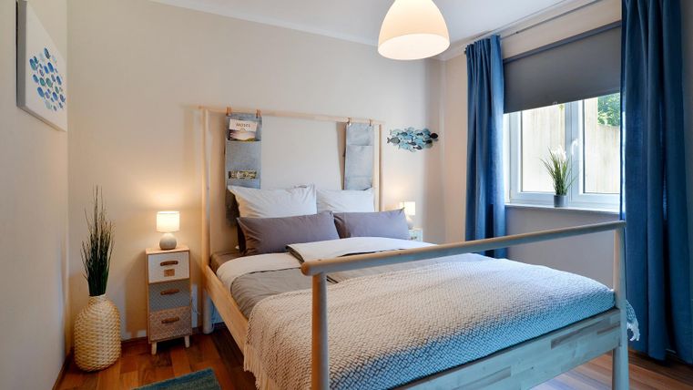 Ein gemütliches Schlafzimmer mit einem Holzbett und weichen Kissen. Das Zimmer hat große Fenster und ist mit blauen Vorhängen dekoriert.